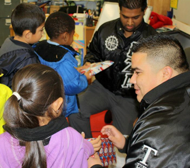 two CSUEB students giving toys to elementary school children.