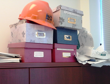 a messy desk with hard hat, boxes and papers.